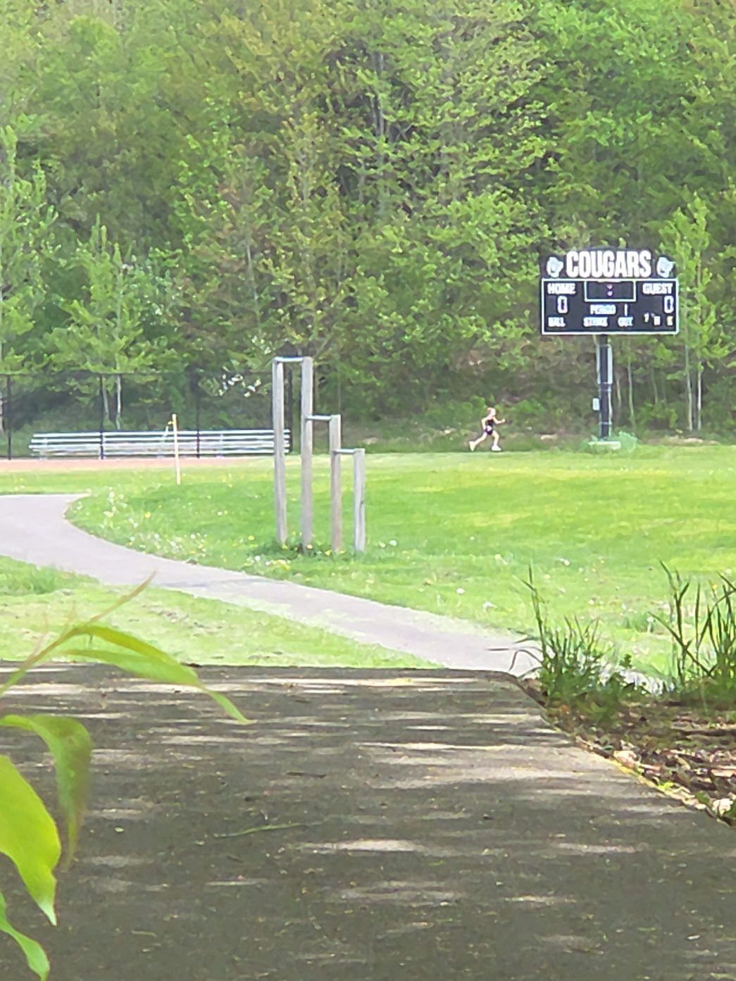 A paved walking trail with a sign that says 'Cougars' in the distance and a person running