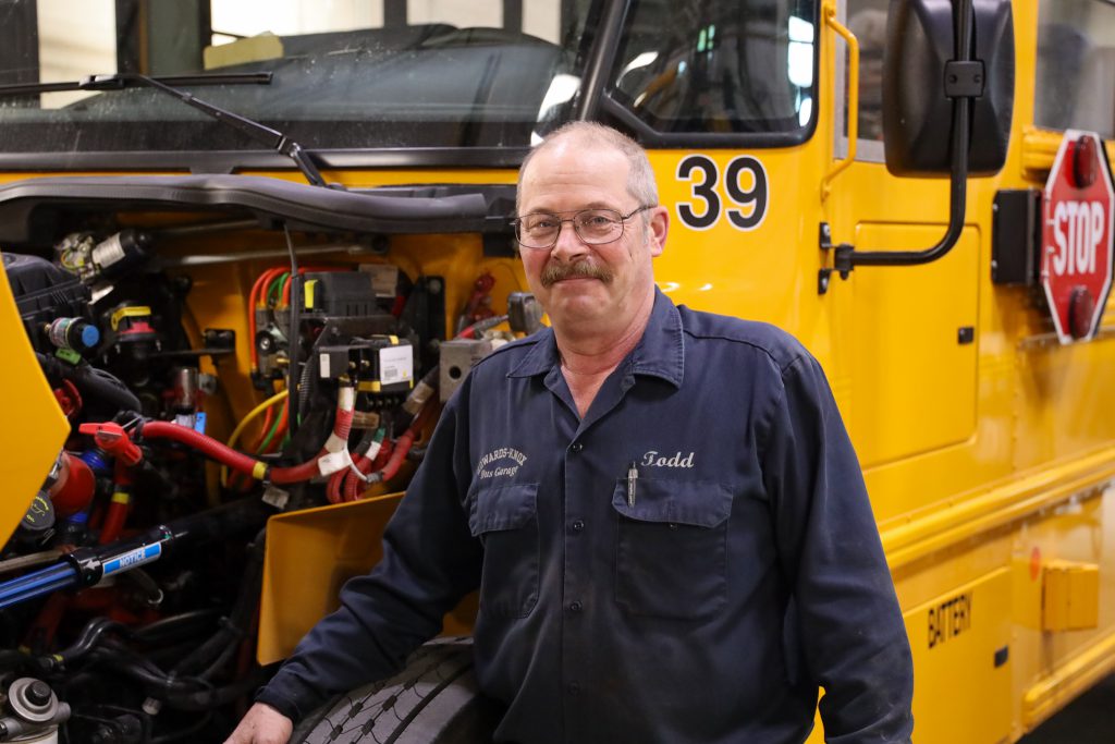 A man standing next to a school bus with its engine hood open