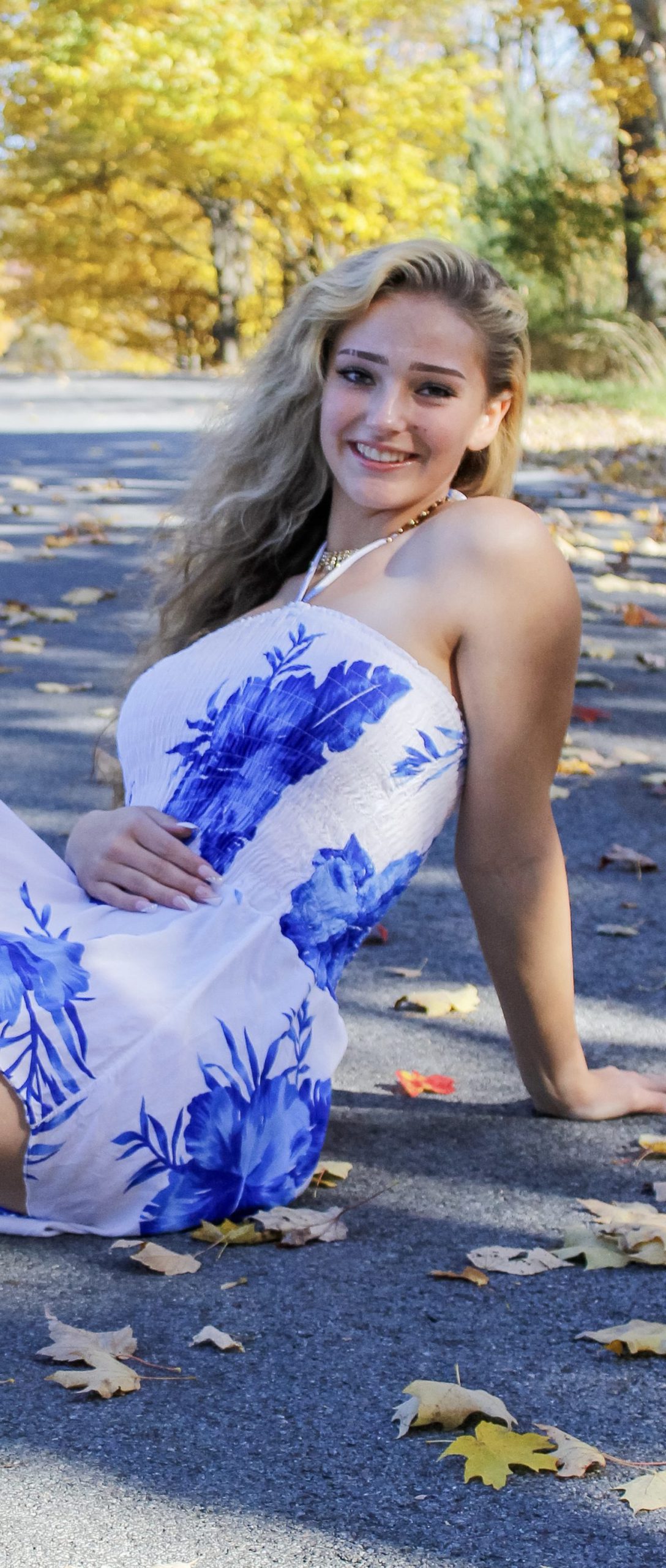 A student posing for a photo on a paved surface with trees in the background