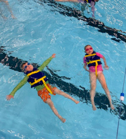Two students wearing life jackets floating in pool