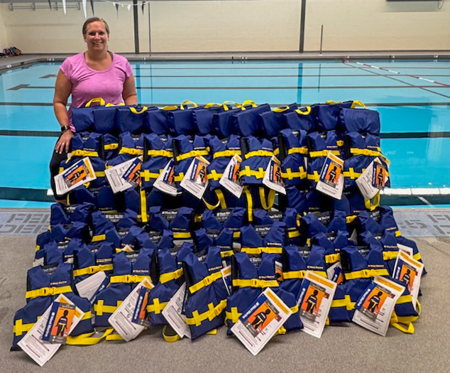 A woman standing next to a display of life jackets near a pool