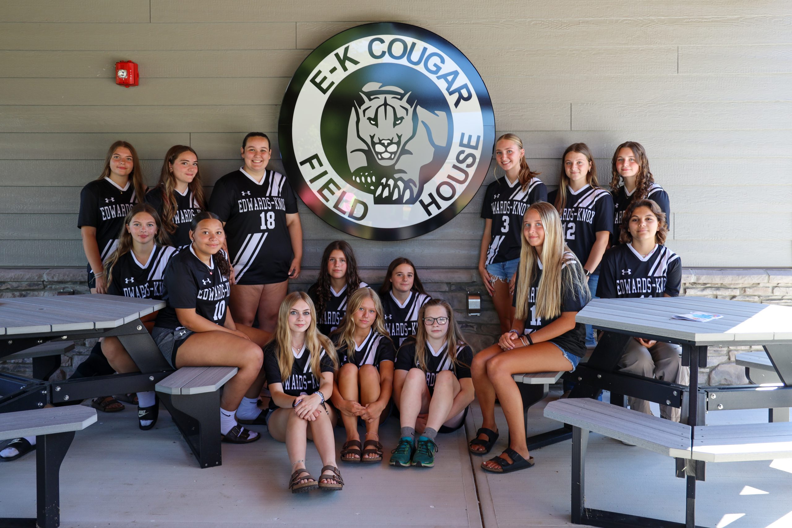 A team of student-athletes sitting near a sign that says 'E-K Cougar Field House'