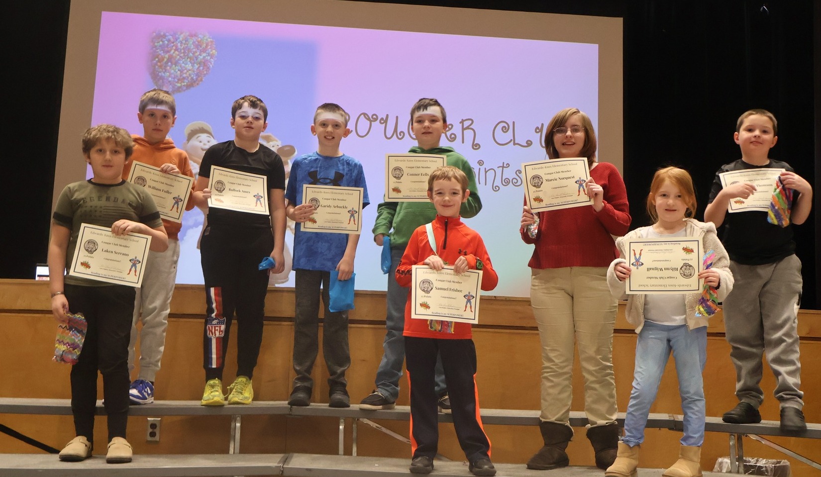 Small group of elementary students standing on risers holding certificates
