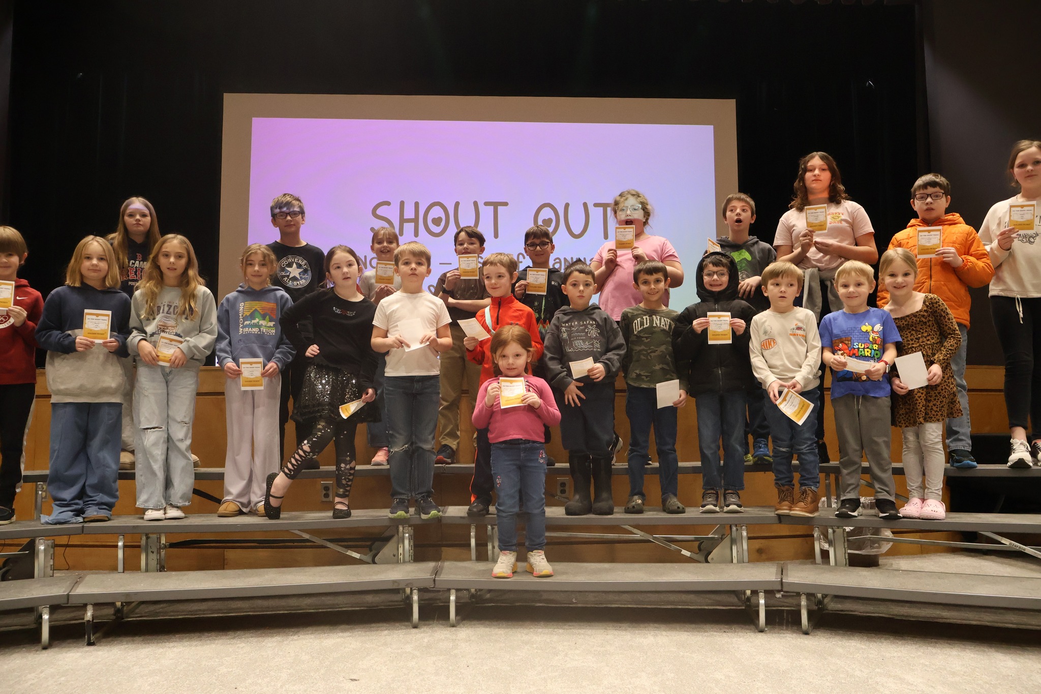 Large group of elementary students standing on risers holding certificates