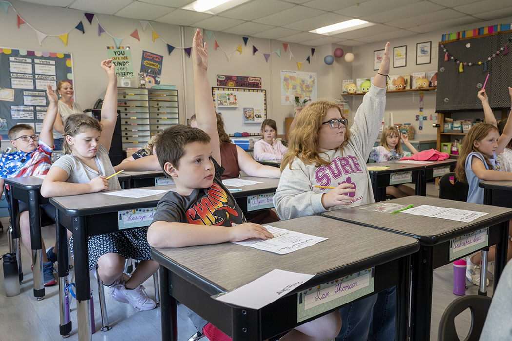 Students in a classroom raise their hands.
